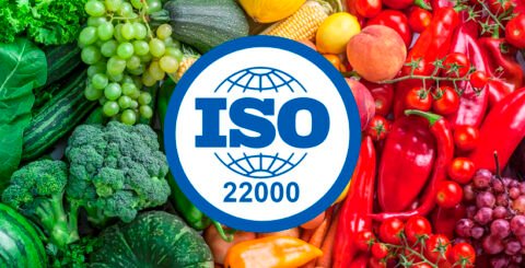 Φωτογραφία με φρούτα και λαχανικά στο παρασκήνιο και μπροστά το λογότυπο του "ISO 22000".